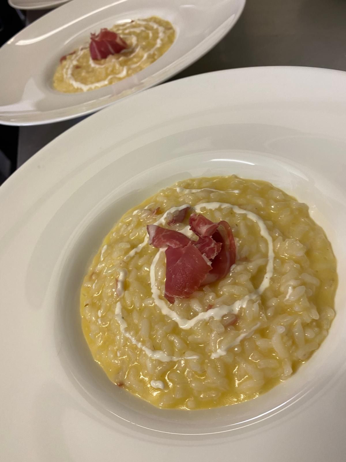 Risotto in ciotole bianche, guarnito con panna e prosciutto.