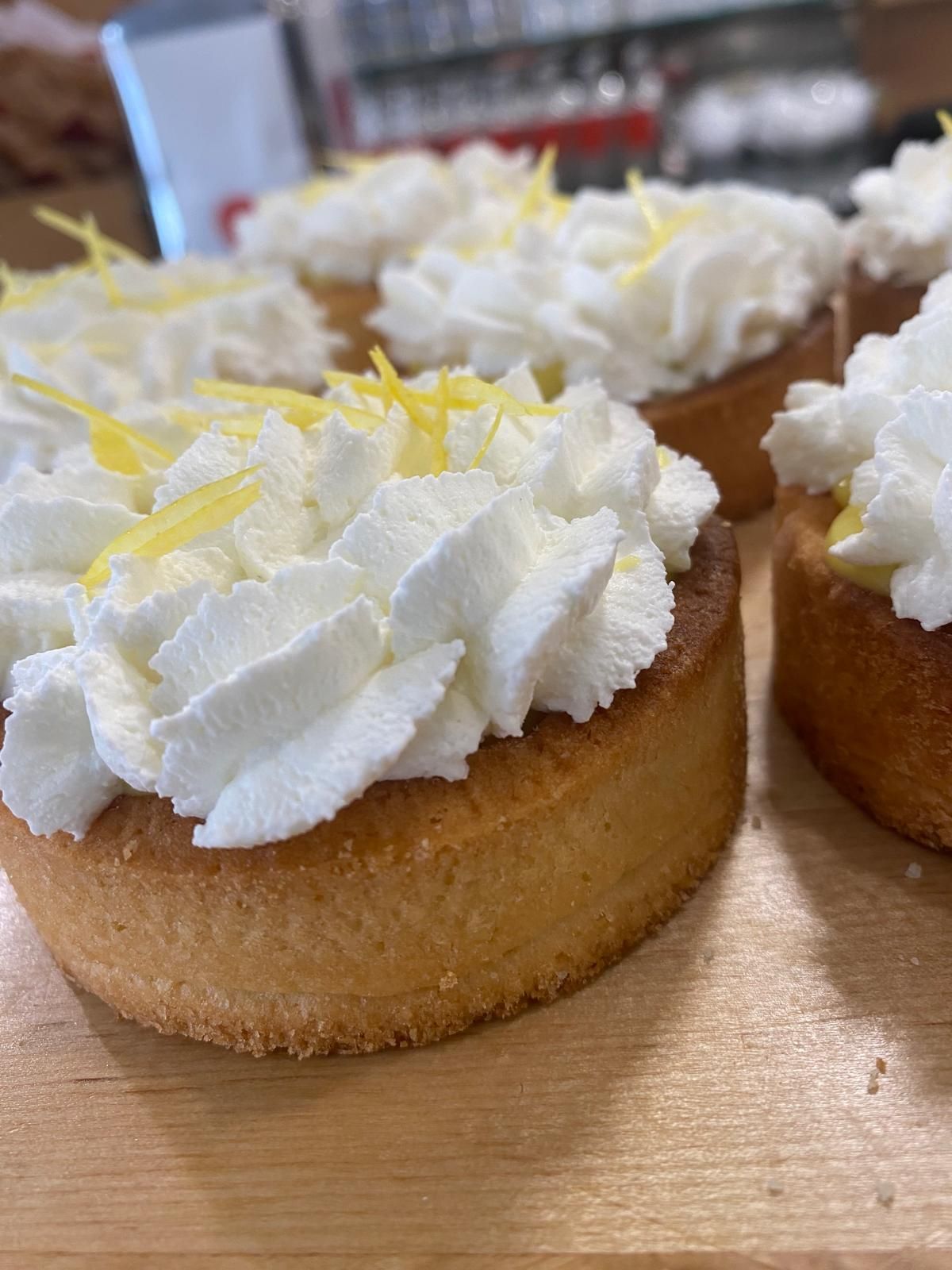 Crostatine al limone con panna montata bianca e scorza di limone su una superficie di legno.