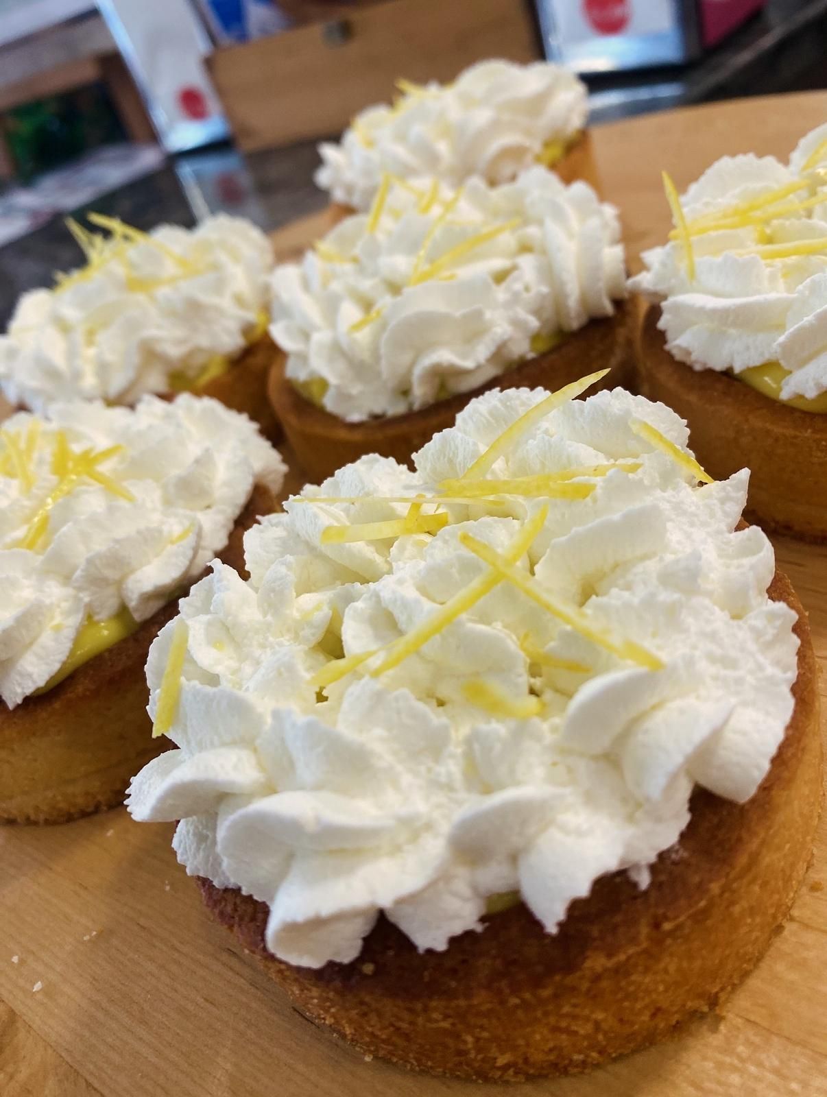 Crostatine di crema al limone guarnite con panna montata e scorza di limone su una superficie di legno.