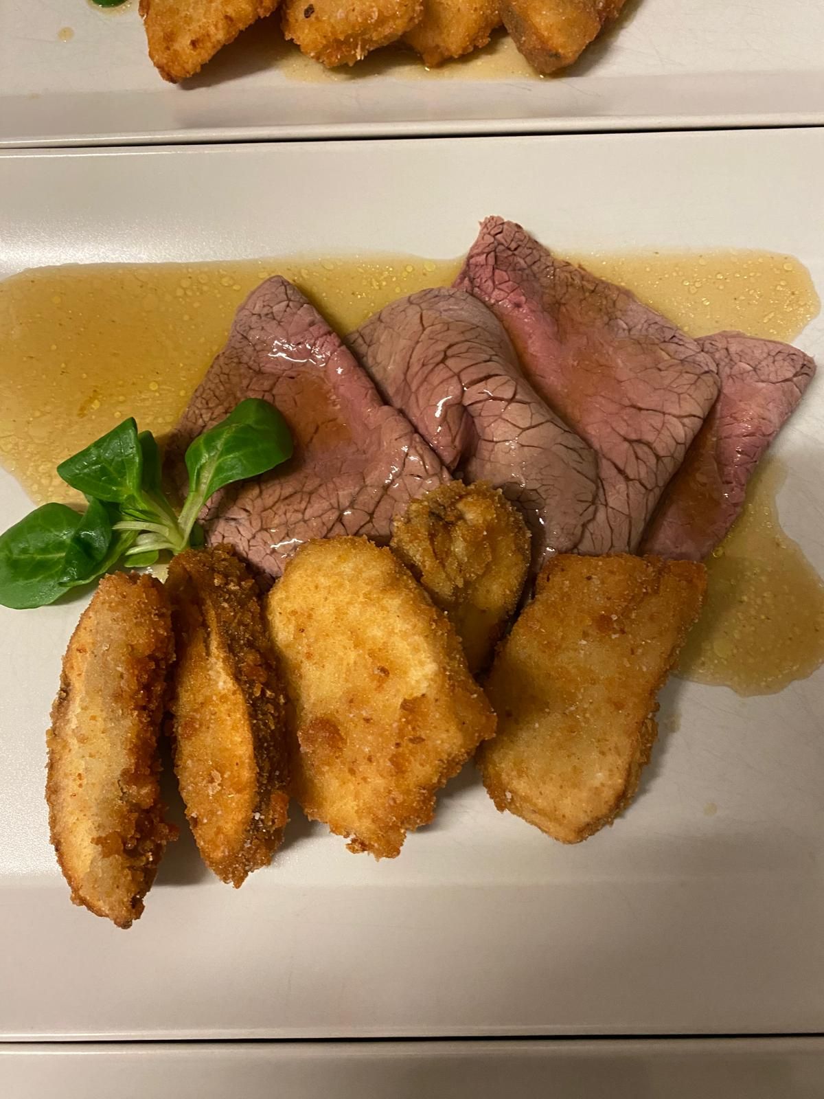 Roast beef affettato con salsa, patate fritte e verdure su un piatto bianco.