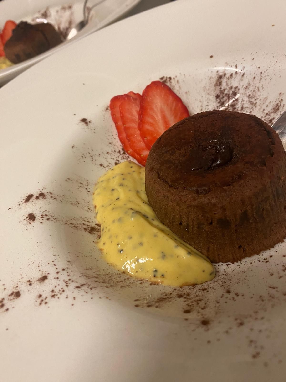 Torta al cioccolato fuso con crema pasticcera e fragole su un piatto bianco cosparso di cacao.
