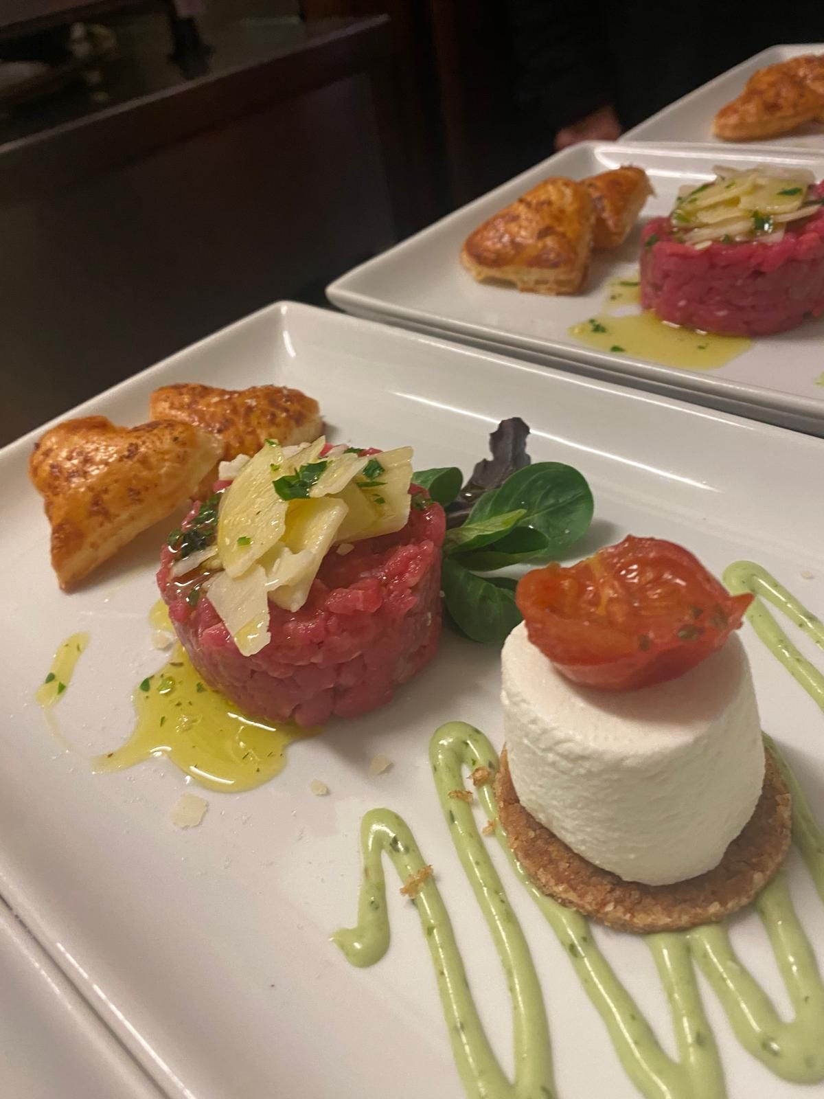 Due piatti con cibo gourmet: tartare di manzo, formaggio, pasta sfoglia, verdure e salsa.