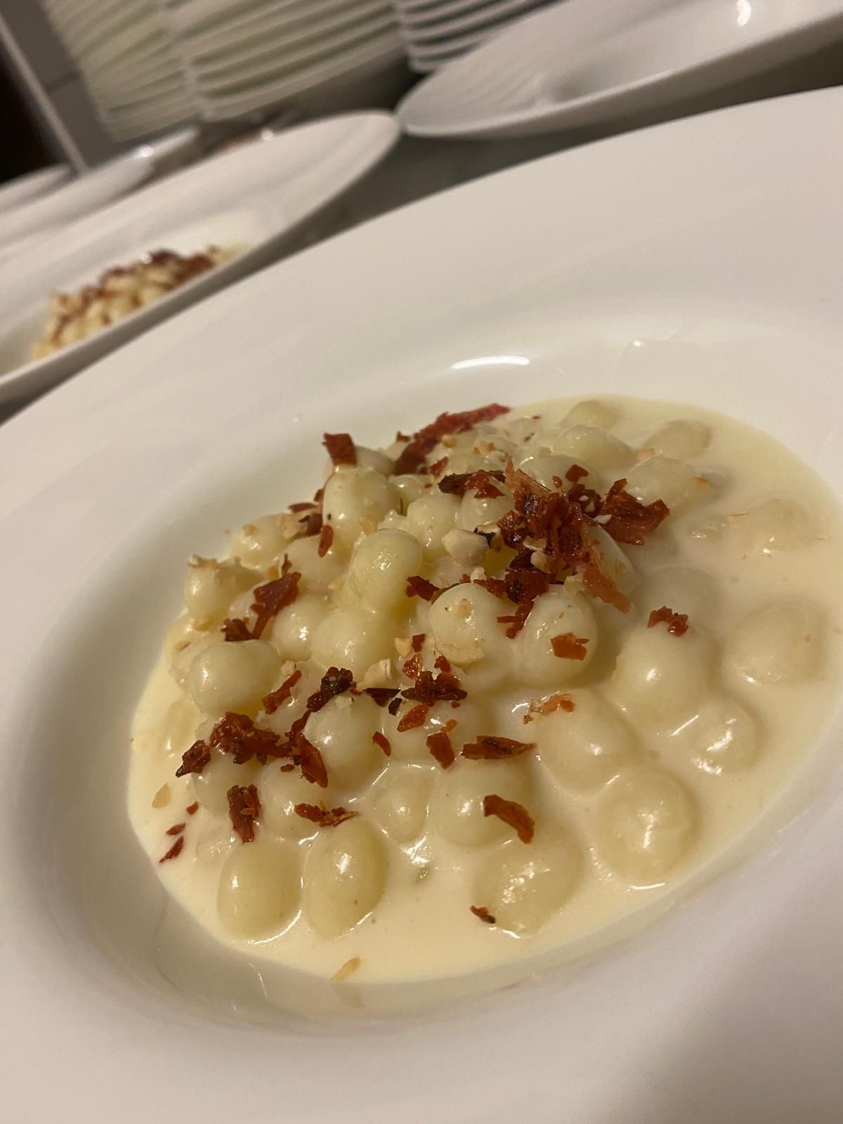 Gnocchi in salsa cremosa, guarniti con pezzetti di pancetta, serviti in una ciotola bianca.