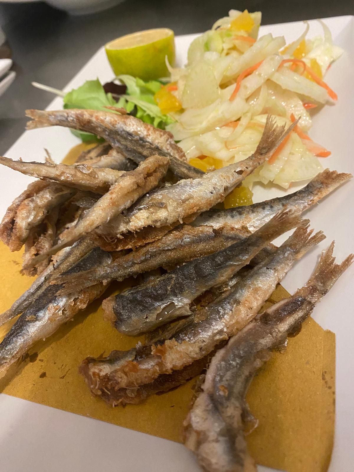 Pesce fritto disposto su un piatto con insalata e spicchio di lime.