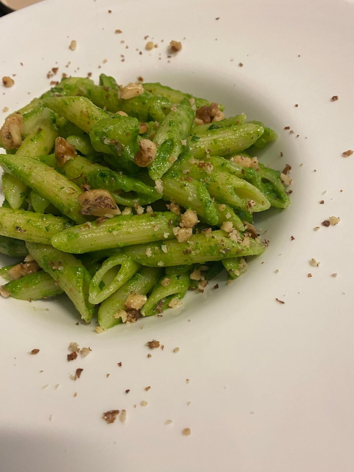 Pasta con pesto verde e noci in una ciotola bianca.