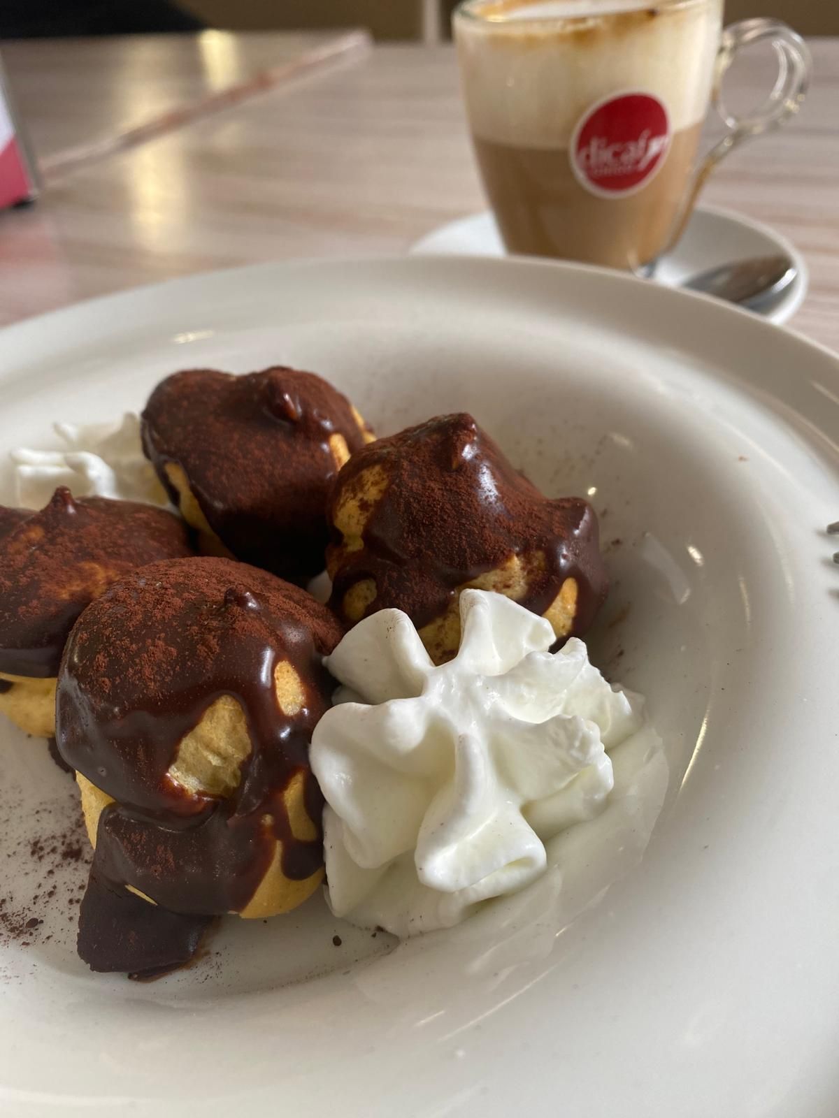 Profiteroles con salsa al cioccolato e panna montata, serviti con un cappuccino.