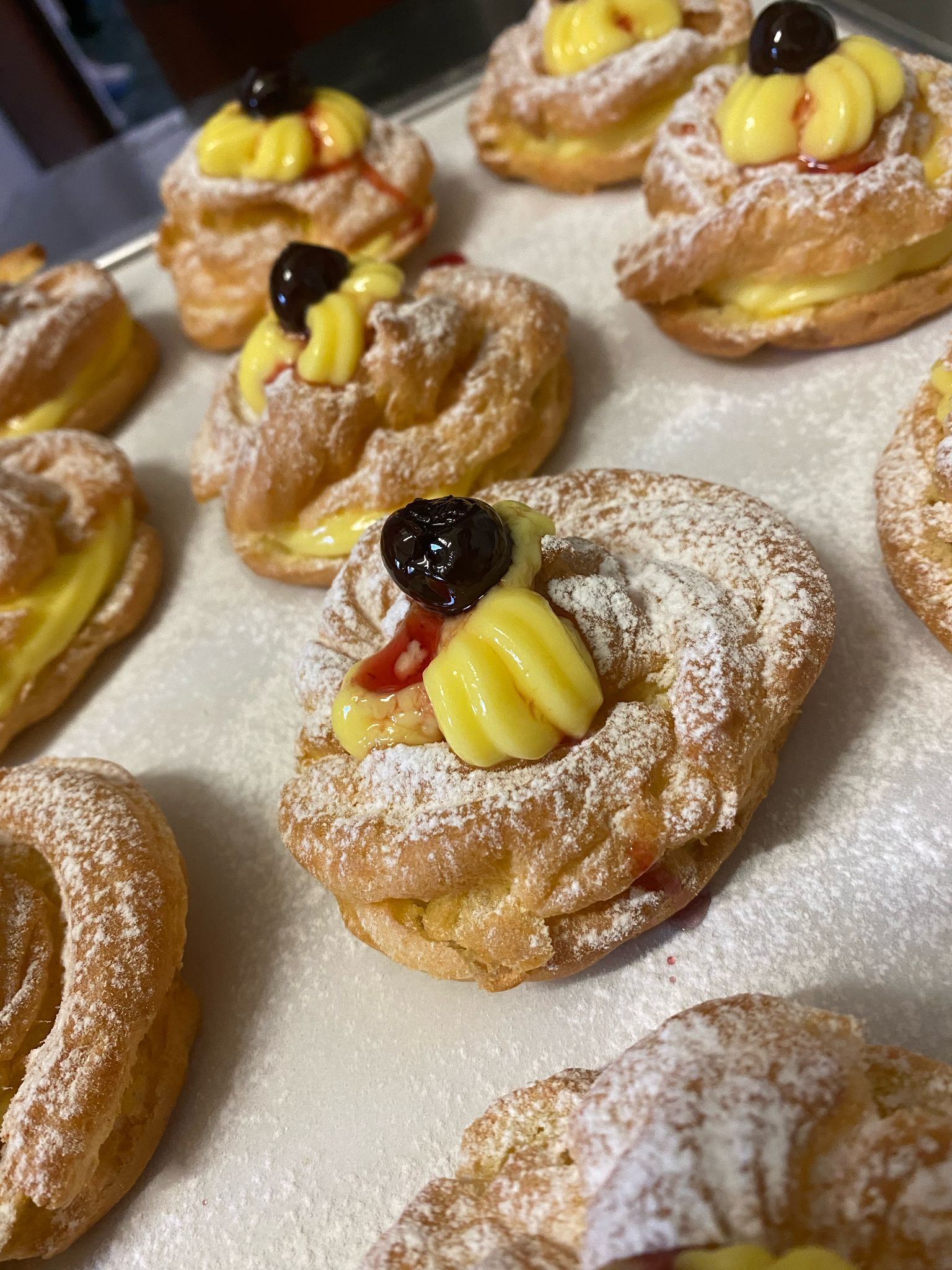 Primo piano di pasticcini su un vassoio, a forma di anello, con ripieno di crema pasticcera, ciliegia e zucchero a velo.