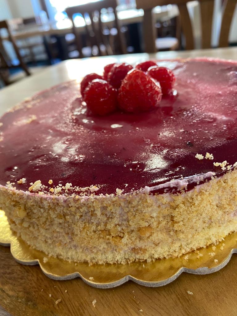 Torta glassata al lampone con lamponi freschi sopra, servita su un piatto con bordo dorato smerlato.