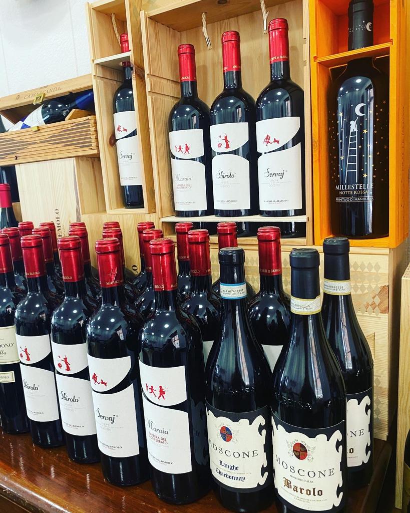 Bottiglie di vino con tappi rossi su scaffali di legno in un negozio.