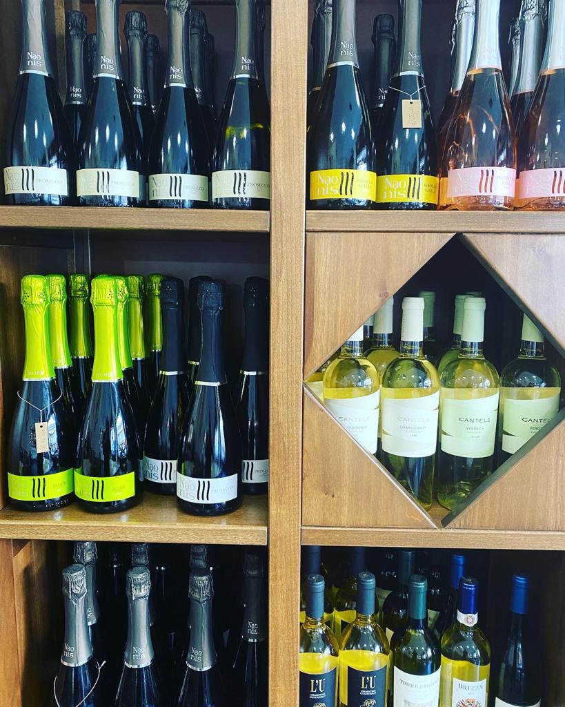 Scaffali pieni di bottiglie di vino di vario tipo in un negozio, molte delle quali con etichette colorate.