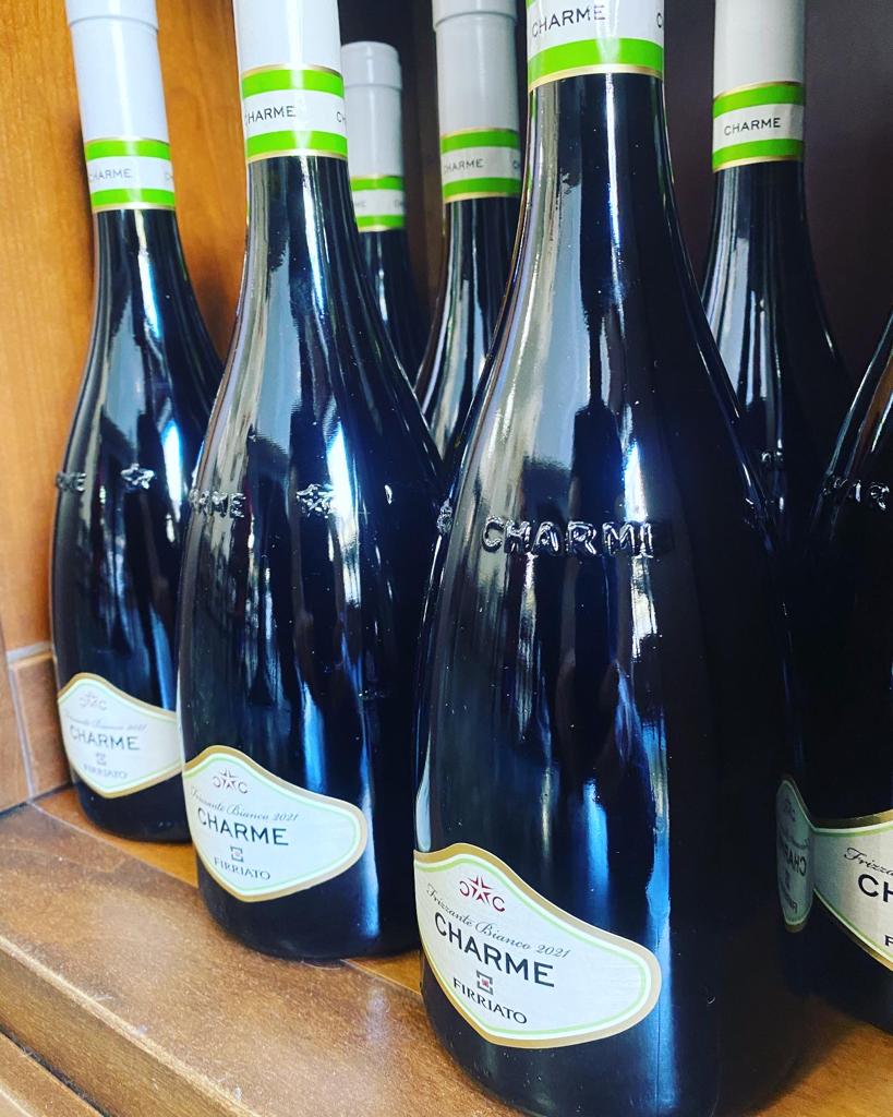 Diverse bottiglie di vino scuro con etichette bianche e verdi sono disposte vicine l'una all'altra.