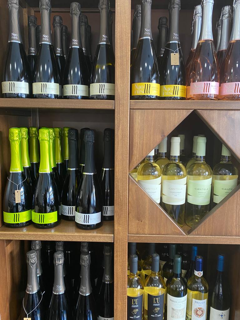 Scaffali pieni di bottiglie di vino di vario tipo, tra cui spumanti e fermi, esposti in una vetrina di legno.