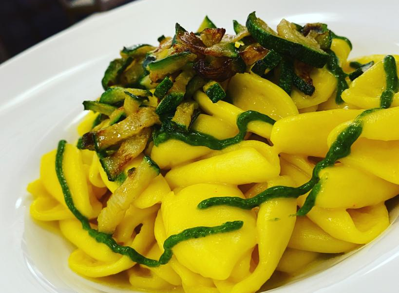 Piatto di pasta con salsa gialla e contorno di zucchine.