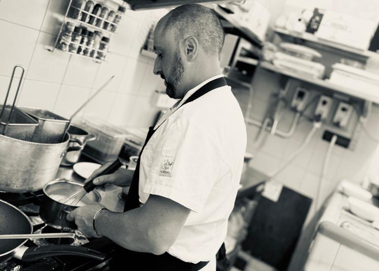 Cuoco in uniforme bianca che mescola una pentola sui fornelli in cucina.