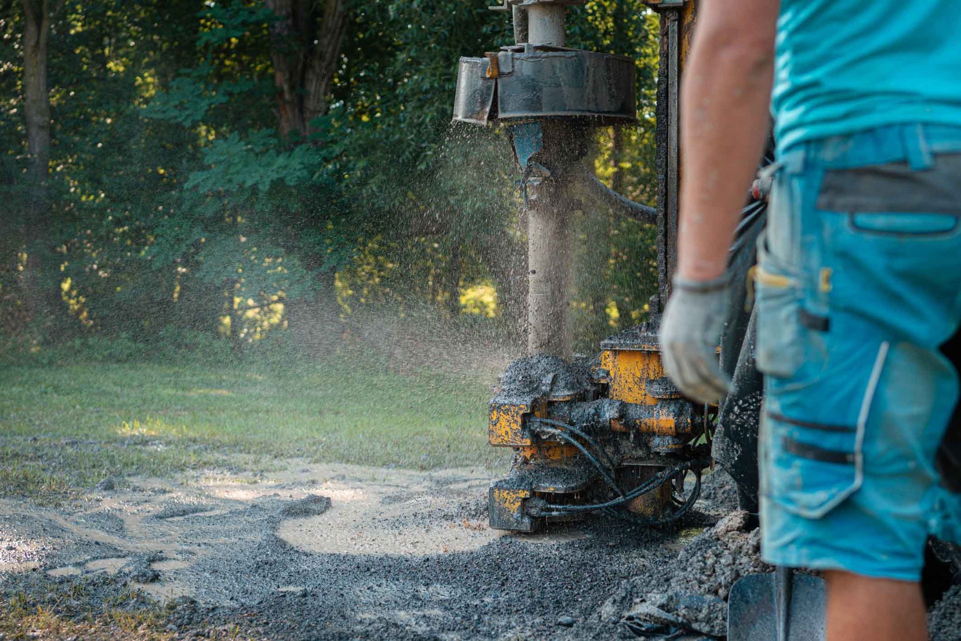 Photograph showing a close-up of a drilling rig operating on a grassy area with water and mud spraying from the drill bit. Photograph showing a close-up of a drilling rig operating on a grassy area with water and mud spraying from the drill bit.