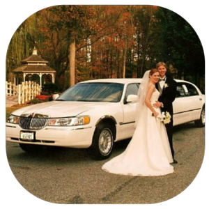 Bride and groom posing beside a white limousine on a tree-lined road