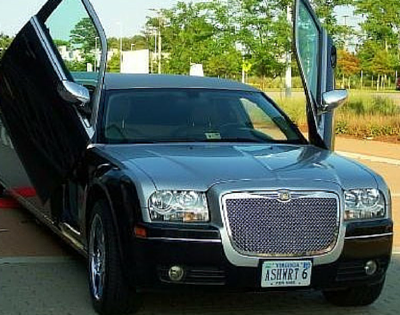 Black luxury car with gullwing doors raised, parked outdoors.