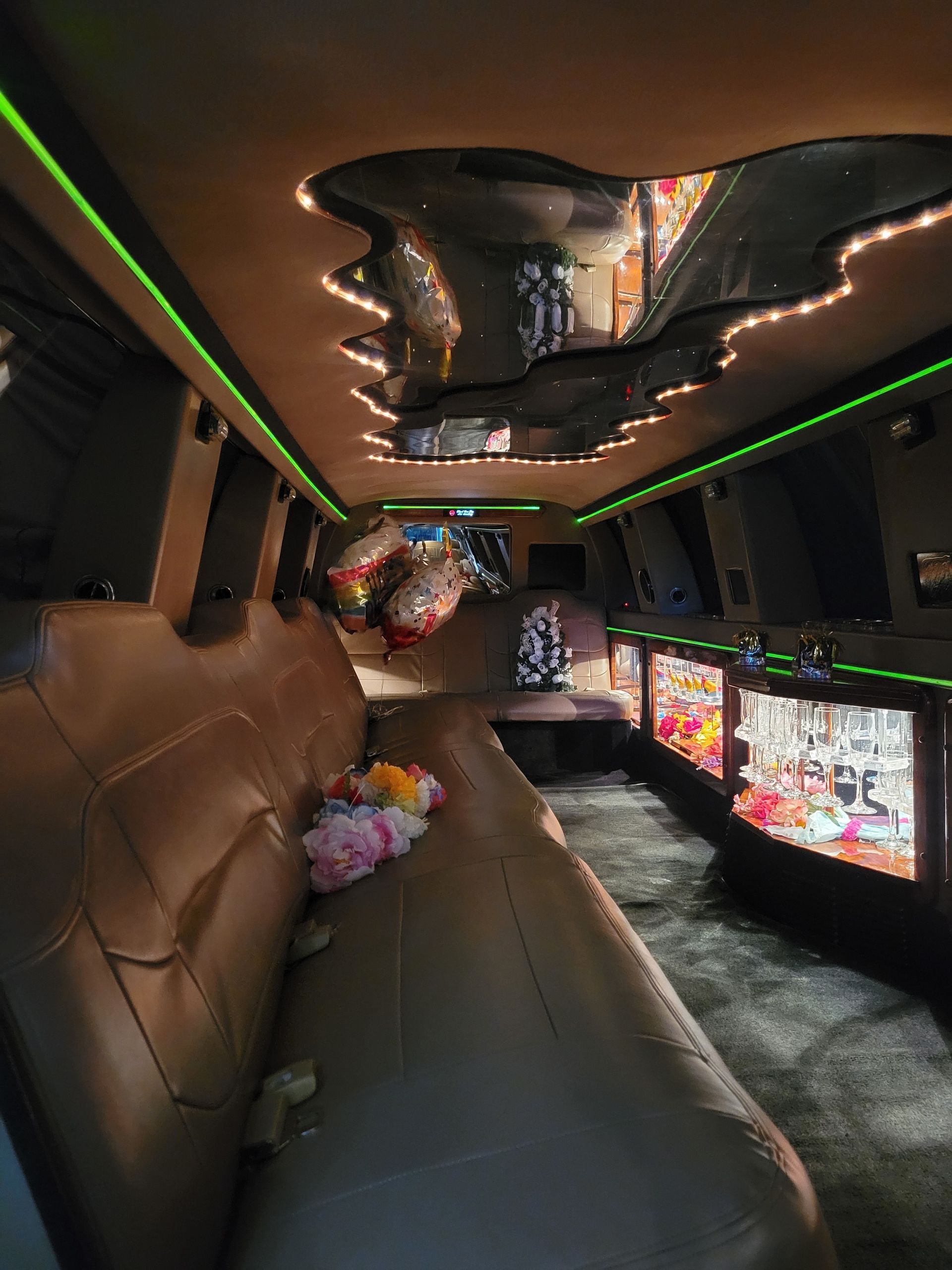 Luxury limousine interior with tan leather seating, neon ceiling lights, and colorful floral decor