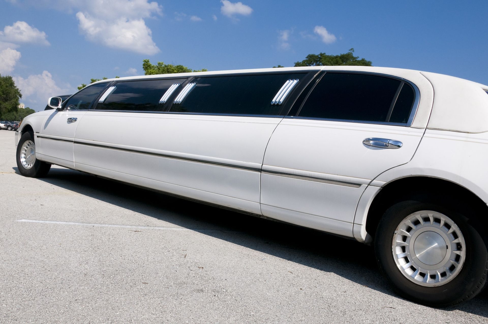 White stretch limousine parked on a sunny roadside under a blue sky