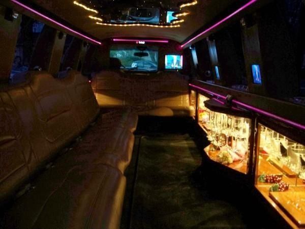 Dim limousine interior with brown leather seats, neon lighting, and a bar cabinet with drinks.
