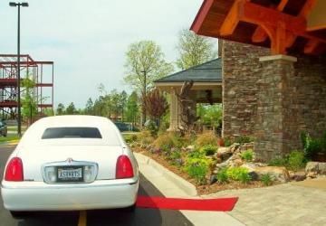 White sedan at a hotel entrance under a red canopy, beside a stone building and landscaped curb.
