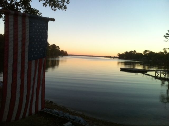 Sunset over a calm lake with an American flag hanging on the left and a dock on the right