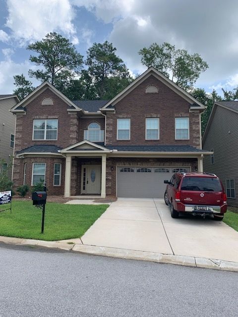 Two-story brick house with a two-car garage, red SUV, and a driveway in a suburban neighborhood.