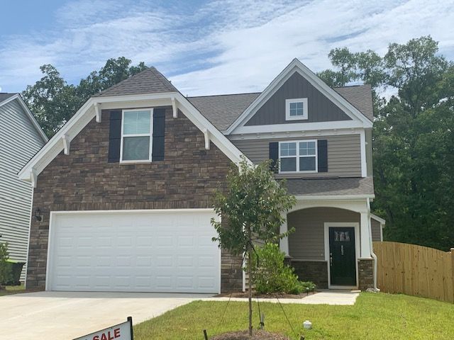 Two-story suburban house with brick and siding, white garage door, front porch, and a small “For Sale” sign.