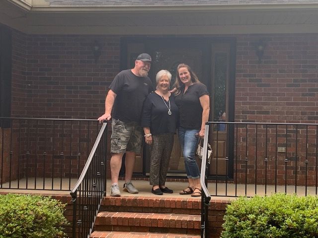 Three people standing on brick front steps outside a house, smiling at the camera.