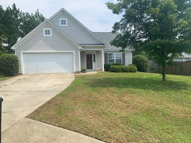 Suburban house with white garage, front porch, and sloped driveway beside a grassy lawn