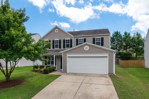 Two-story suburban house with a two-car garage, driveway, lawn, and trees under a blue sky.