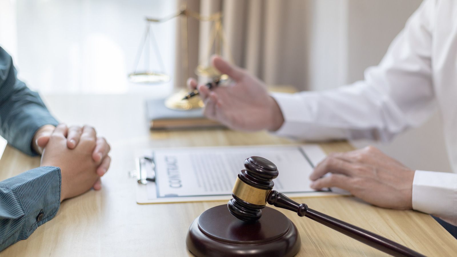 Lawyer meeting with client, hands clasped across desk, gavel and documents in foreground
