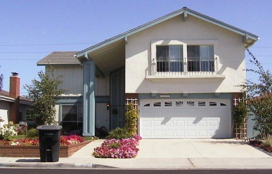 Two-story house with white stucco walls, blue accents, a two-car garage, and a driveway with flower beds.