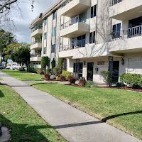 Apartment building with balconies and a sidewalk. Green lawn and trees.
