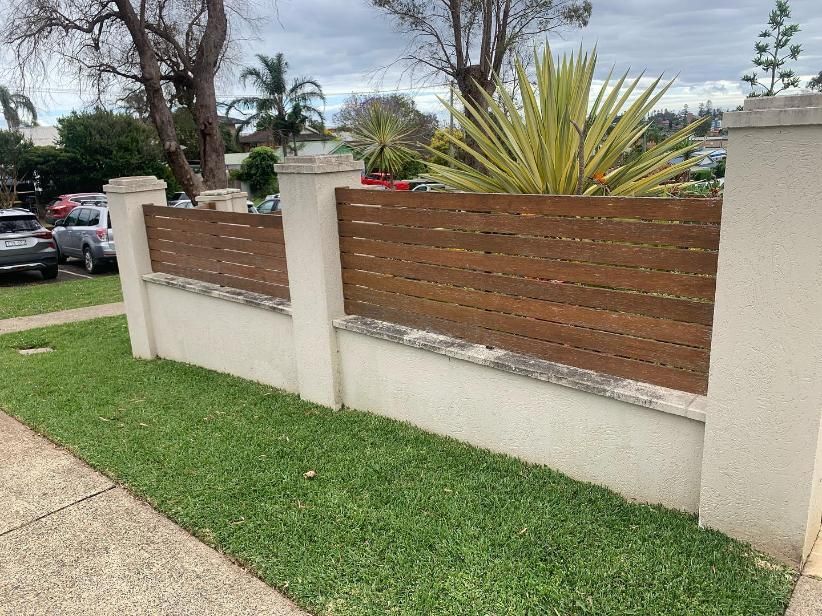 A Wooden Fence is Surrounded by a White Wall and Grass — Holster Painting Contractors In Port Macquarie, NSW 