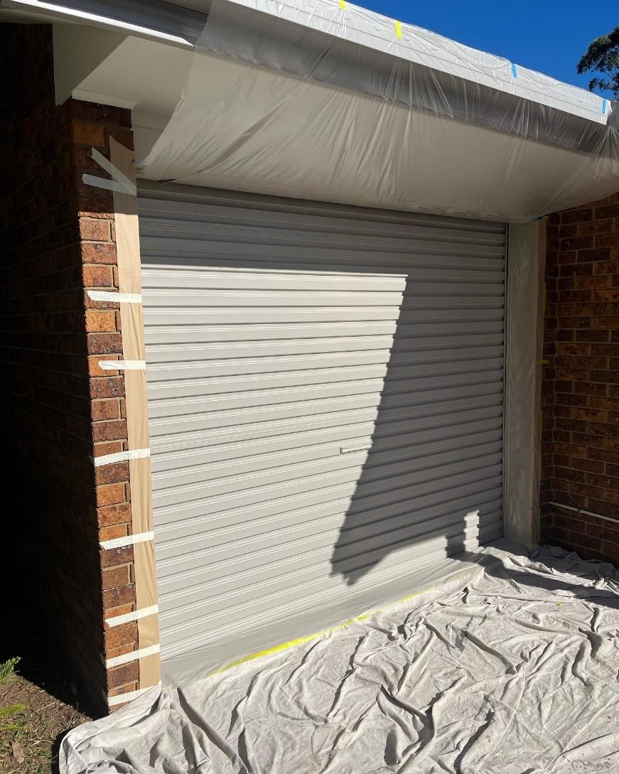 A White Garage Door is Being Painted on a Brick Building — Holster Painting Contractors In Port Macquarie, NSW 