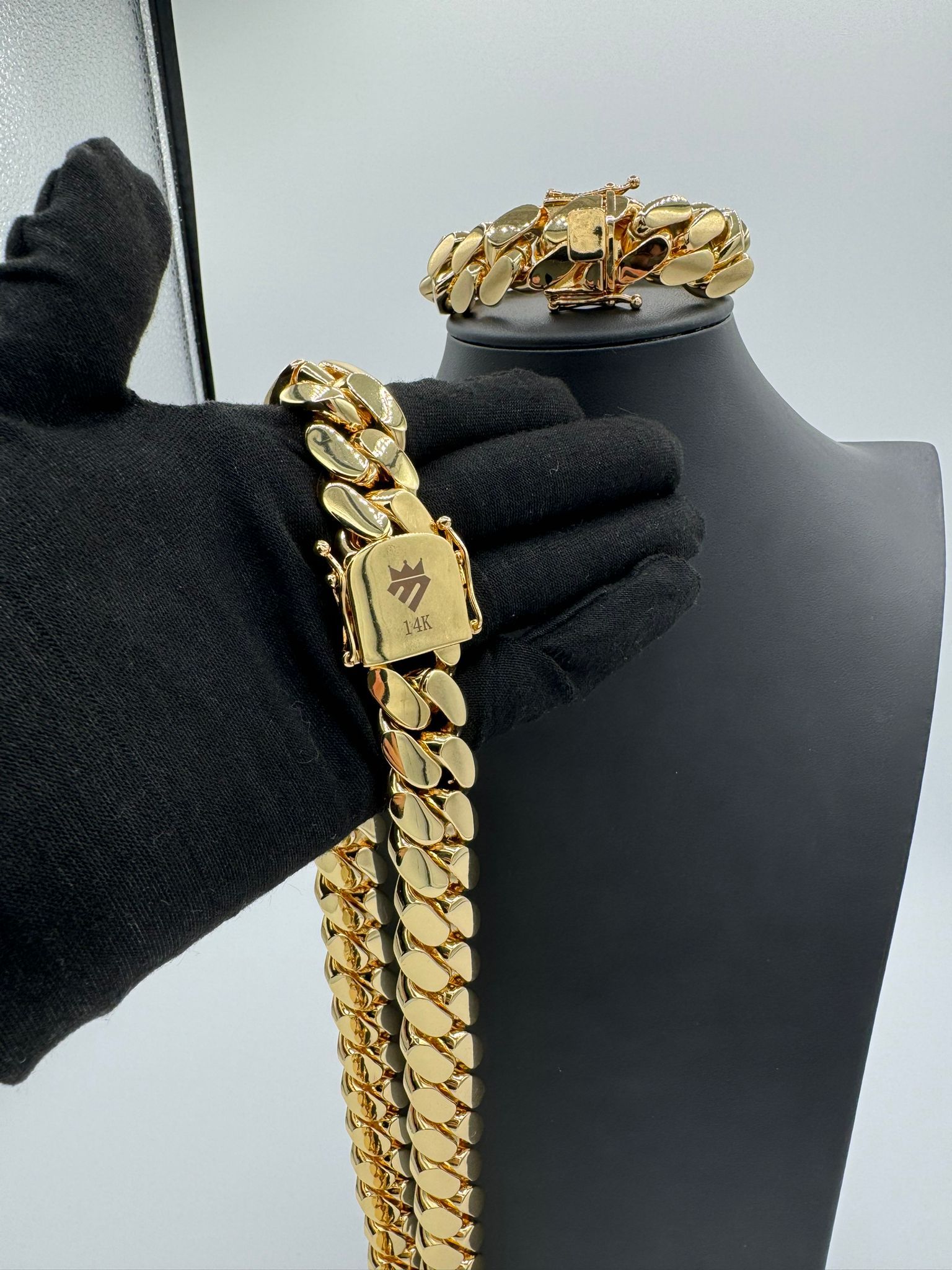 A person is holding a gold chain and bracelet on a mannequin.