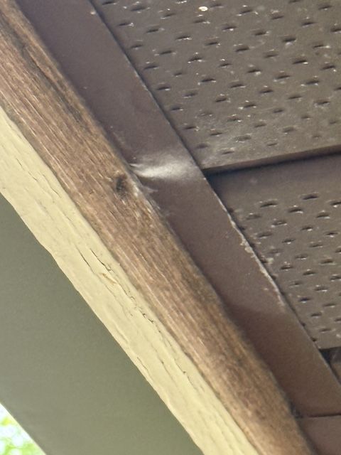 Close-up of a wooden roof beam and perforated soffit panel with a small damaged spot