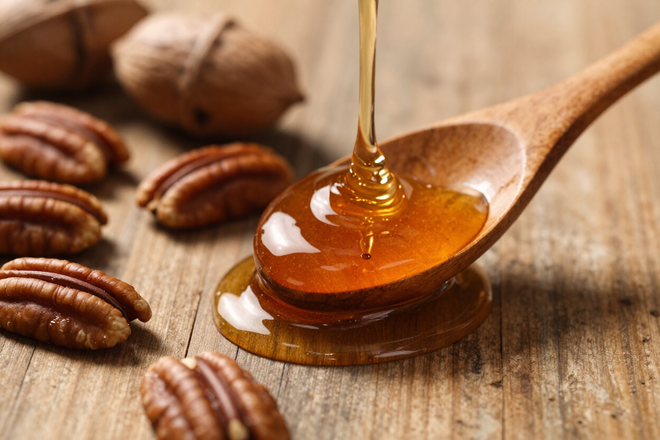 Honey dripping onto a wooden spoon with pecans on a rustic tabletop