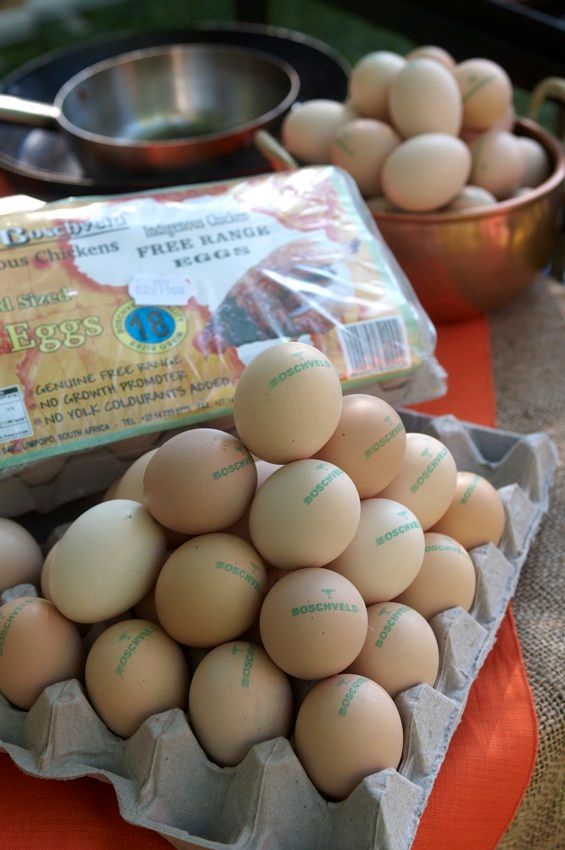 Carton of brown eggs with more eggs in bowls and a package on a table