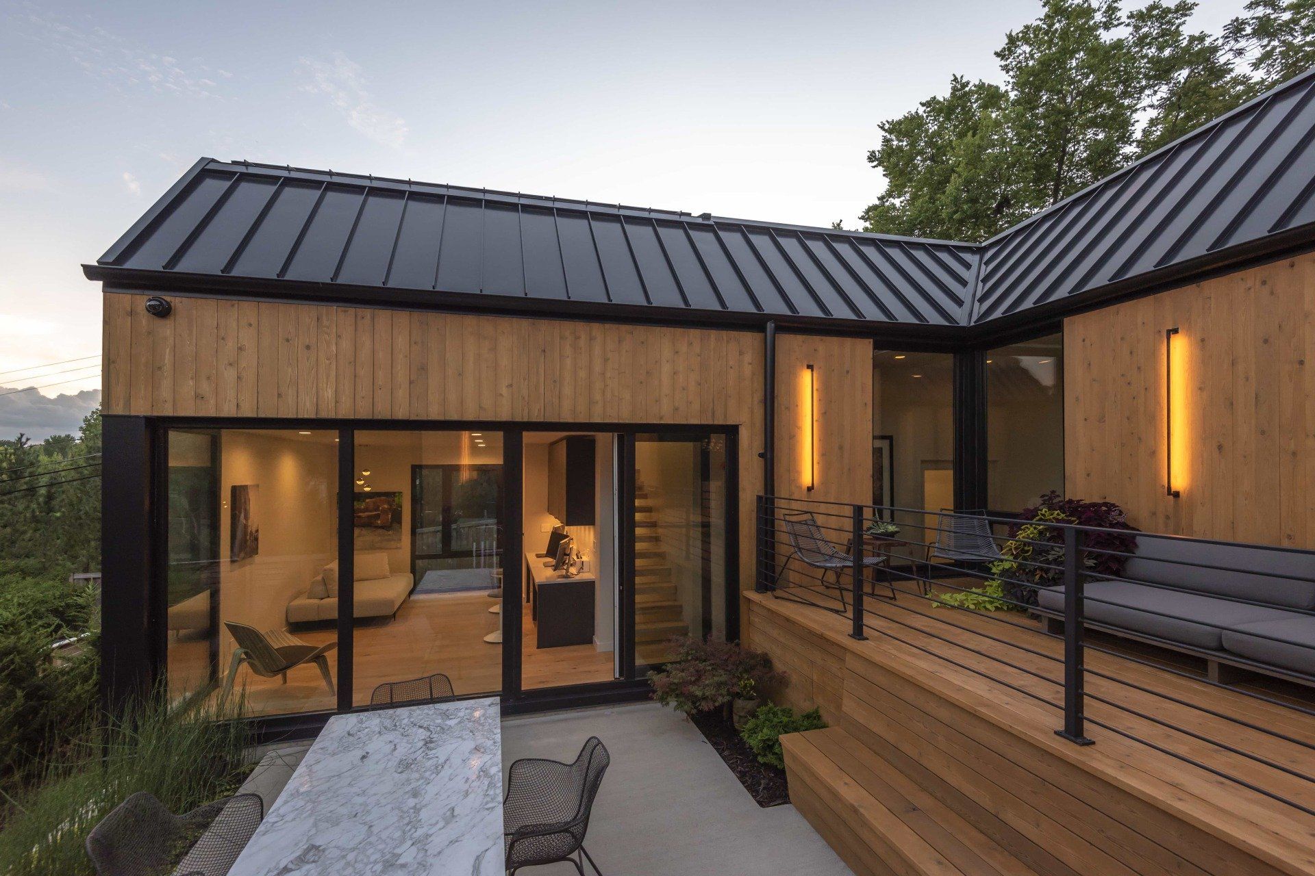 Modern home exterior with wood siding, black roof, deck, and outdoor seating.