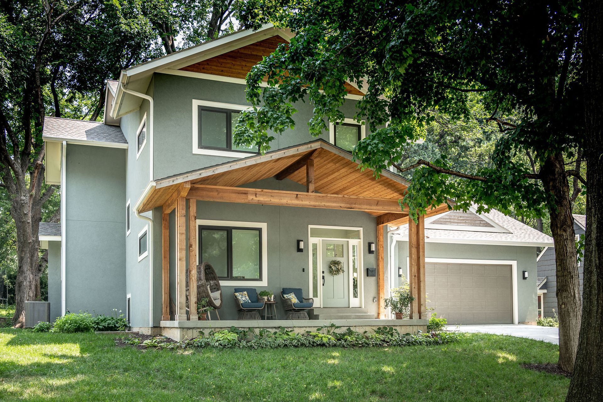 Modern two-story house with gray stucco exterior, wooden porch, and a detached garage.