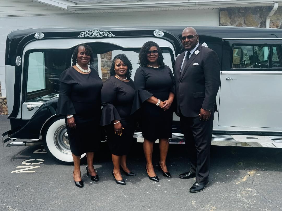 Four people in black formalwear pose beside a black-and-white limousine outdoors.