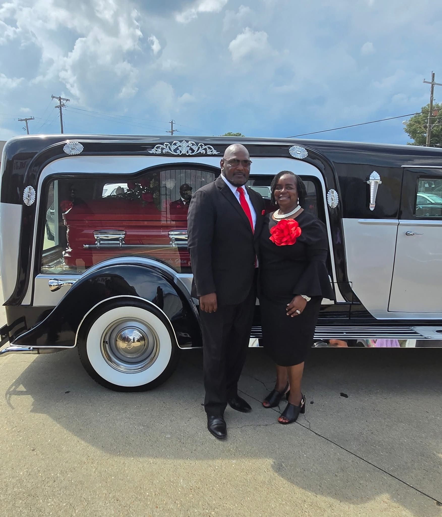 Couple posing beside a black vintage car outdoors on a sunny day