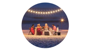 Un grupo de personas está sentada alrededor de una mesa en la playa por la noche.