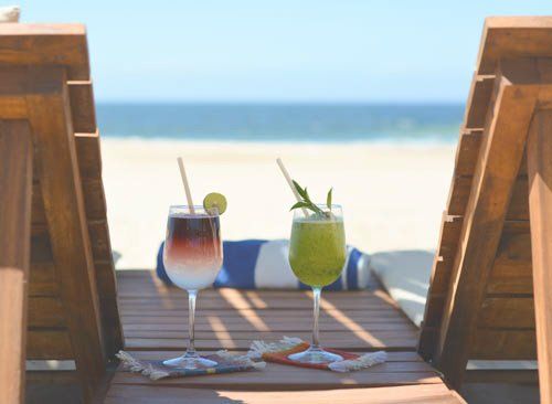 Dos bebidas están sentadas en una mesa de madera en la playa.