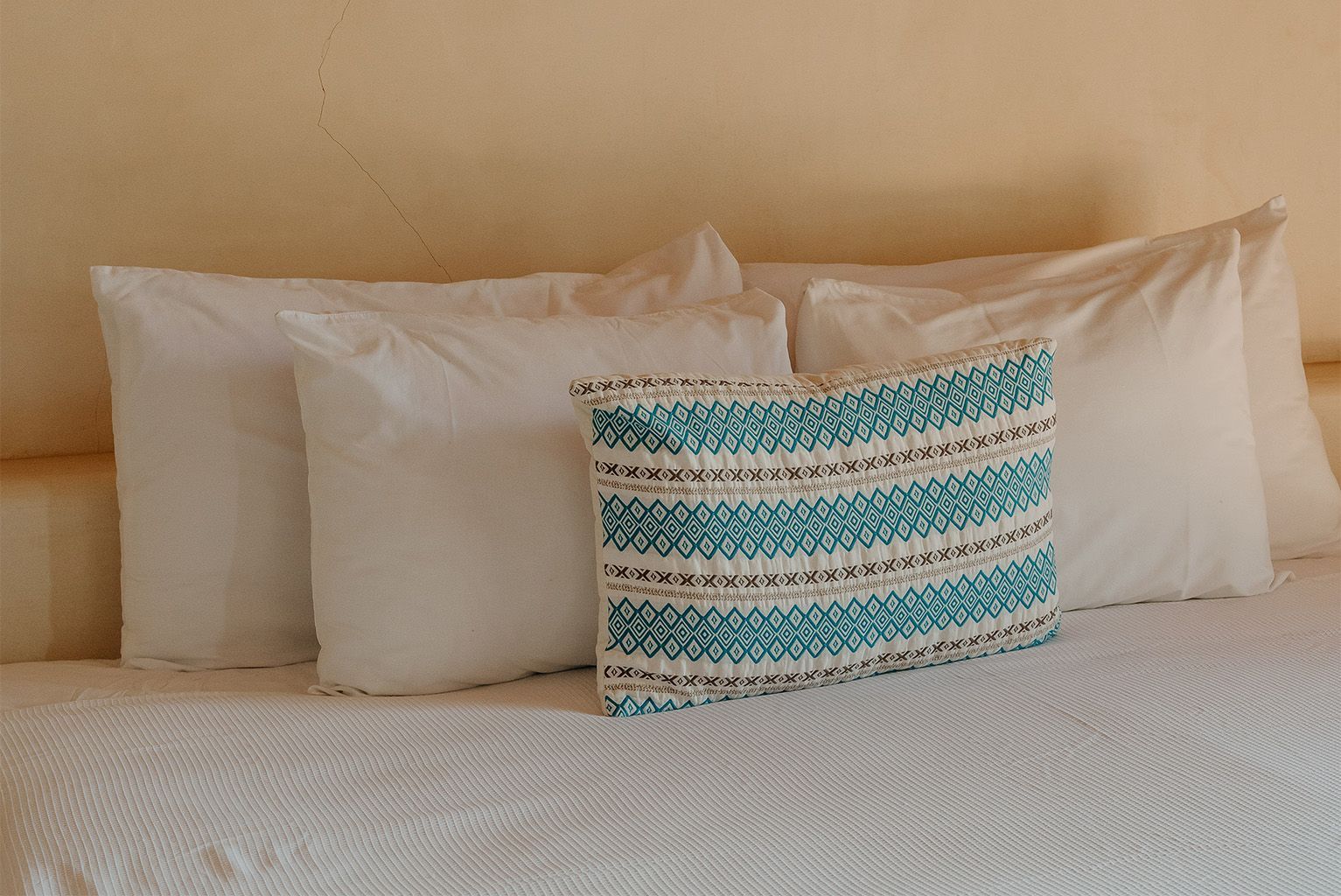 Una cama con sábanas blancas y una almohada azul encima.