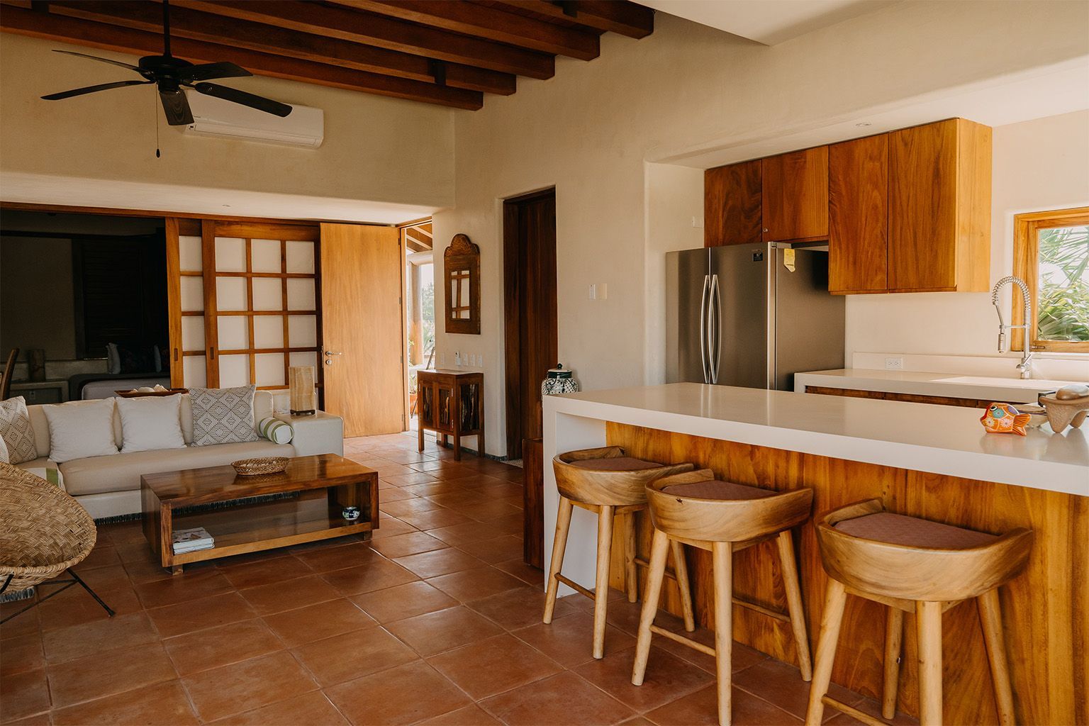 Una sala de estar con sofá, mesa, taburetes y una cocina con ventilador de techo.