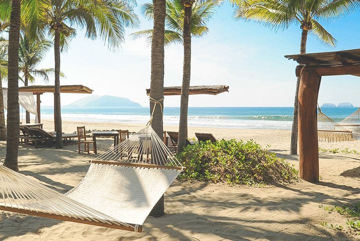 Una hamaca cuelga entre dos palmeras en una playa.