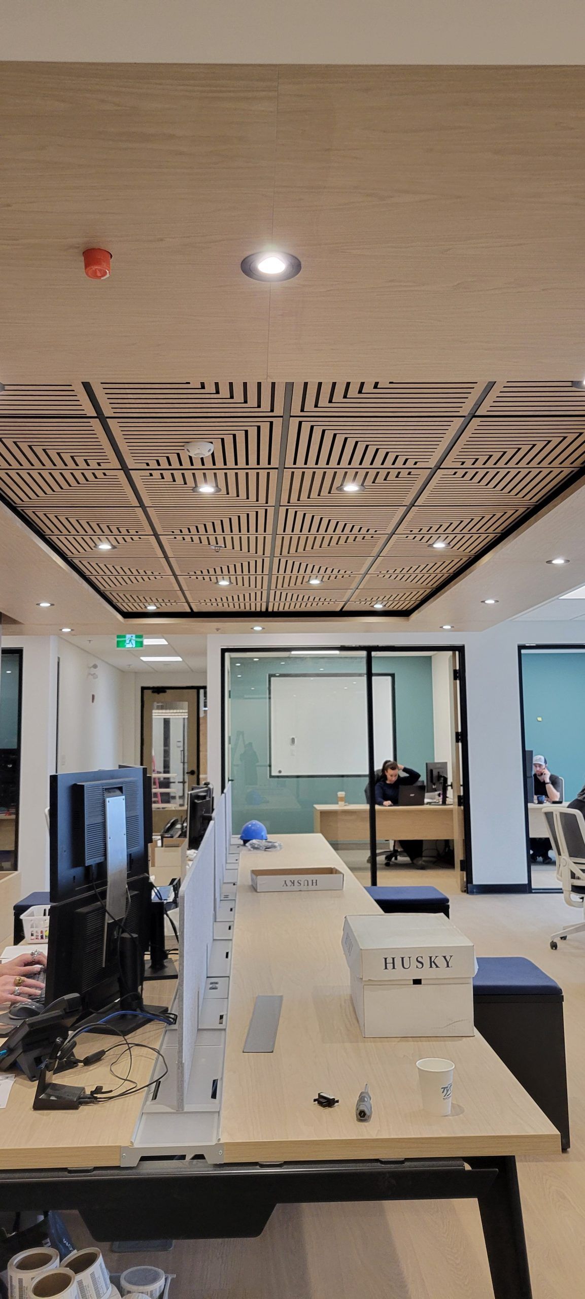 Un bureau ouvert avec une longue table, des ordinateurs et un plafond décoratif. Une personne travaille en arrière-plan.